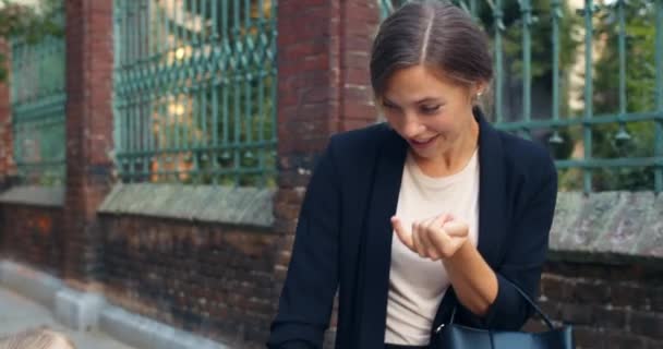 Alegre hermosa mamá contando junto con su hija pequeña mientras camina por la calle. Joven mujer caminando de la mano con su hermoso hijo, hablando y sonriendo en su camino a la escuela . — Vídeos de Stock