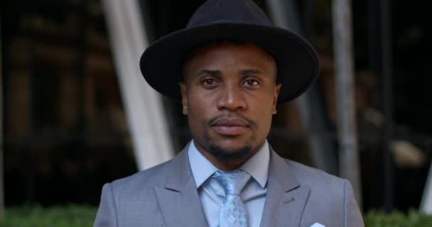 Portrait of stylish guy in hat and suit looking to camera while standing at street. Close up view of handsome african american man in 30s wearing tie posing. Concept of real life. — Stock Video