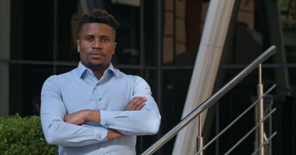 Portrait d'un chef d'équipe masculin ou d'un homme d'affaires prospère debout près d'un centre de bureau moderne.Beau afro-américain croisant les bras et regardant vers la caméra avec une expression faciale sérieuse . — Video