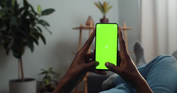 Hombre africano escribiendo mensaje en la pantalla simulada con marcadores de trecking. Chico usando el teléfono inteligente y charlando en las redes sociales mientras está acostado en el sofá. Concepto de croma key y pantalla verde . — Vídeos de Stock