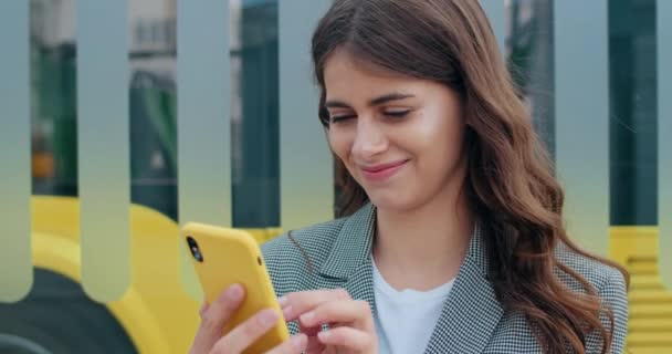 Close up view of millennial woman touching and looking at smartphone screen at city street. Happy girl using phone while browsing internet or reading message and smiling.Outdoors. — Stock Video