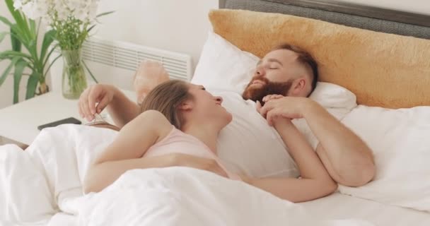 Retrato de casal alegre bonito deitado na cama no início da manhã, falando e sorrindo. Mulher bonita e seu marido bonito ter bom tempo. Conceito de família e relacionamento . — Vídeo de Stock