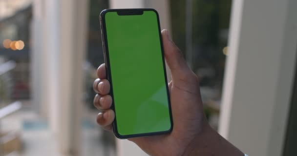 Закройте вид на мужскую руку, прикасающуюся к современному мобильному телефону с приподнятым экраном. Афроамериканец, использующий смартфон. Концепция зеленого экрана и хроматического ключа. Окно на заднем плане . — стоковое видео