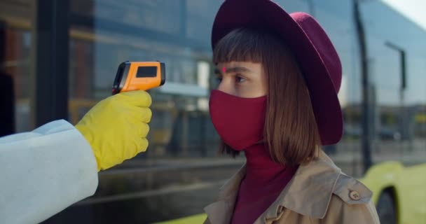 Close-up shot van jonge vrouwelijke reiziger met screening op coronavirus symptomen voor de instapbus. Jonge vrouw op temperatuur controlepunt. Concept van bescherming tegen het coronavirus. Buiten. — Stockvideo