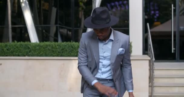 Gelukkige Afro-Amerikaanse zakenman met een draadloze koptelefoon die danst en lacht op straat. Succesvolle knappe man in stijlvol pak en hoed verheugen zich op de overwinning of goed nieuws. Buiten. — Stockvideo