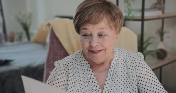 Close-up zicht van lachende vrouw kijken naar foto terwijl ze thuis op stoel zitten.Oudere dame in de 70 met nostalgie tijdens het doorlopen van foto 's. Concept van herinneringen en emoties. — Stockvideo