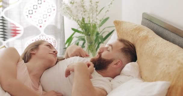 Snygg man och kvinna som kommunicerar och ler när de ligger på sängen. Älskade unga par pratar med varandra och har roligt på morgonen. Begreppet lyckligt förhållande. — Stockvideo
