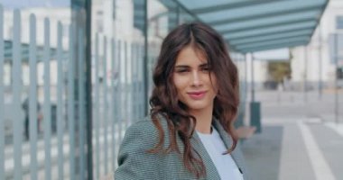 Çekici esmer kadının başını çevirip kameraya baktığı yakın plan görüntüsü. Modern şehrin arka planında dururken poz veren ve gülümseyen bin yıllık güzel iş kadınının portresi.