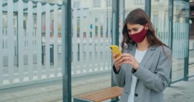 Yeniden kullanılabilir yüz maskeli bir kadın internette geziniyor ya da iş arıyor. Milenyum kızı şehir caddesinde yürürken akıllı telefonunu, kaydırmasını ve dokunmatik ekranını kullanıyor. COVID kavramı.