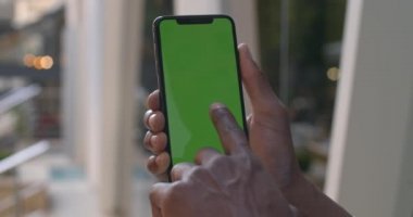 Afro-Amerikan erkek eli, akıllı telefon ekranına dokunuyor. Yeşil ekranlı cep telefonu kullanan adamın yakın görüntüsü. Krom anahtar kavramı. Arkaplanda pencere camı.