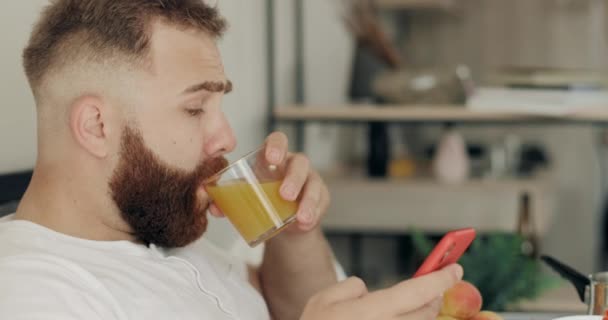 Close up of view przystojny mężczyzna wpisując wiadomość na smartfonie podczas śniadania. Gość z brodą pije sok podczas rozmowy telefonicznej i siedzenia. Pojęcie techniki i czasu wolnego. — Wideo stockowe