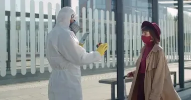 Koruyucu giysiler içinde sağlık görevlisi ve tablet kullanırken kadın yolcuların vücut ısılarını kontrol eden bir maske. Bavullu genç kadın koronavirüs semptomlarına bakıyor..