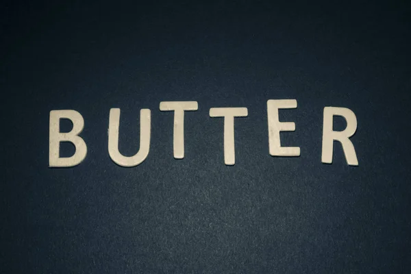青色の背景にカラフルな木製文字で書かれたバター — ストック写真
