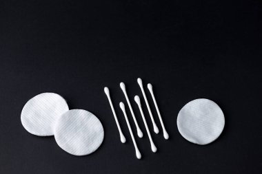 Siyah arka planda pamuk tomurcuklar ve pamuk pedler. Hijyen ürünleri, güzellik aletleri. Üst görünüm, kopyalama alanı, düz uzanma