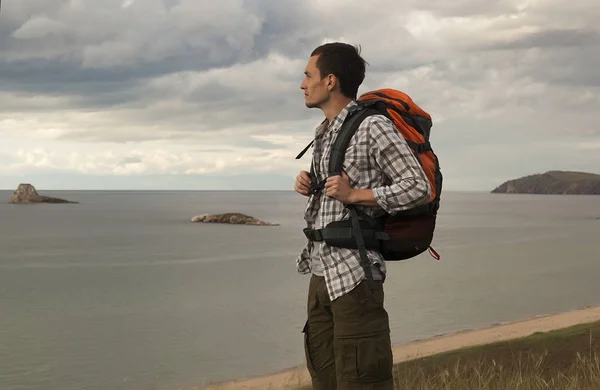 young tourist man with a backpack on the lake, Lake Baikal, summer tourist walk, freedom and happiness, beautiful wildlife