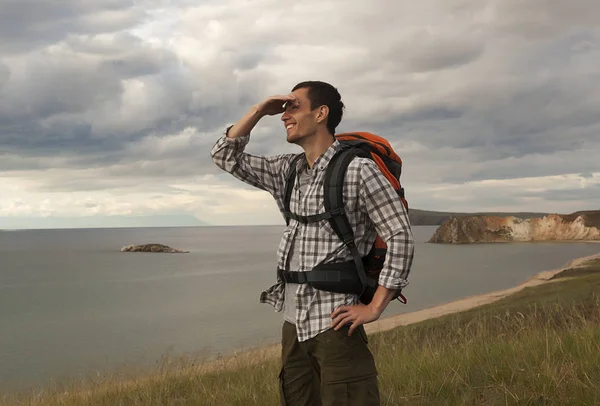 young tourist man with a backpack on the lake, Lake Baikal, summer tourist walk, freedom and happiness, beautiful wildlife