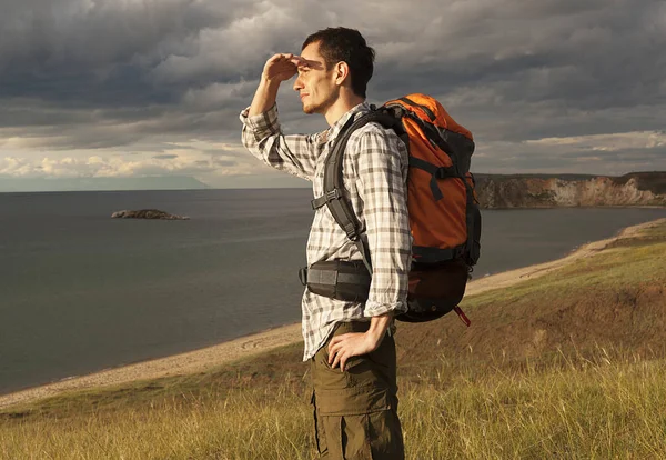 young tourist man with a backpack on the lake, Lake Baikal, summer tourist walk, freedom and happiness, beautiful wildlife