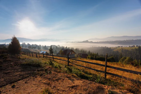 Sonniger und nebliger Morgen in den Bergen. Dorf auf den nebligen Hügeln — Stockfoto