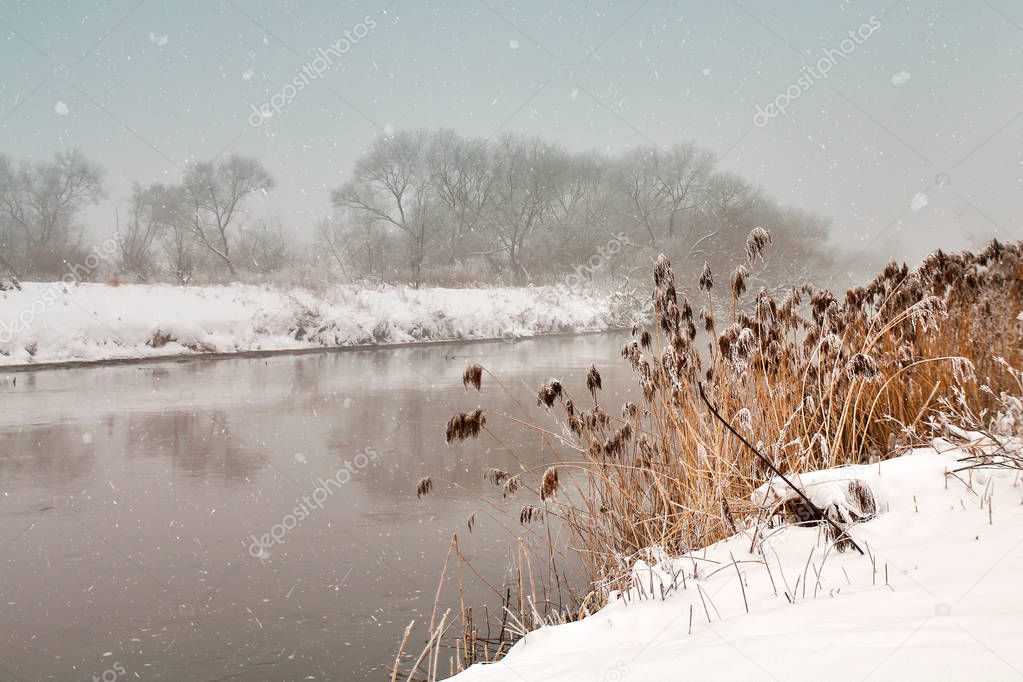 Snowfall over the river. Winter misty cloudy snowy weather.