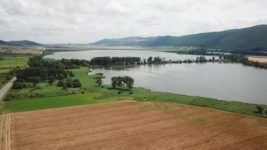 Tarlaları, çayırları, gölü ve dağları olan yaz manzarası. Göl kenarındaki yol. Deponun havadan görüntüsü / Hrhovske Gölü, Rybniky