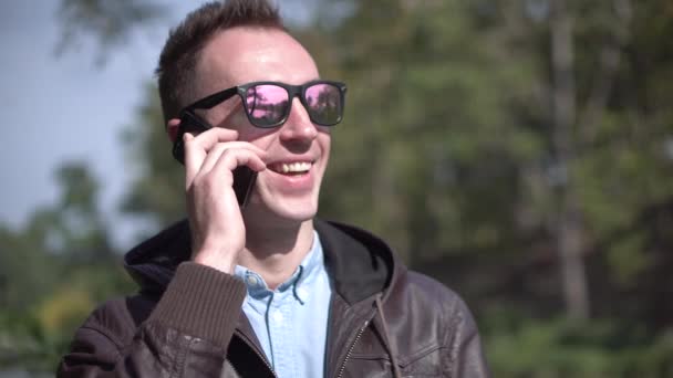 Young attractive happy man in sunglasses talkning by phone — Stock Video