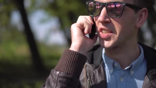 Молодий чоловік в сонцезахисних окулярах розмовляє по телефону — стокове відео