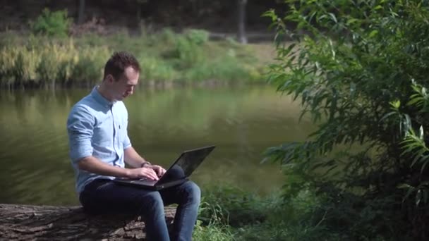 Jovem homem atraente trabalhando no computador no parque — Vídeo de Stock