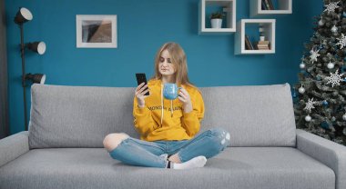 Elinde telefon ve bardak tutan kız.