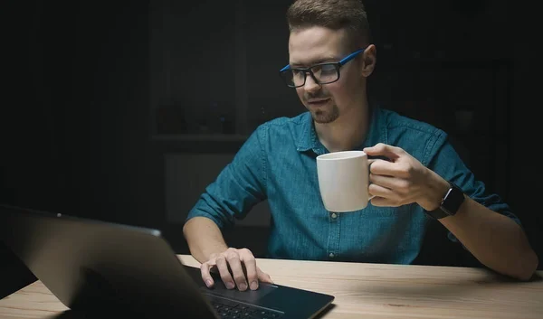 Guy holding cup looking at laptop — 스톡 사진