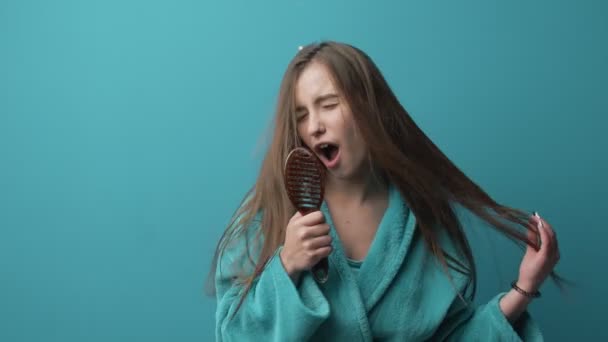 Attractive girl in warm bathrobe using comb for singing song — 비디오