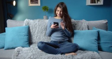 Kanepede otururken telefonu kullanan esmer kadın.