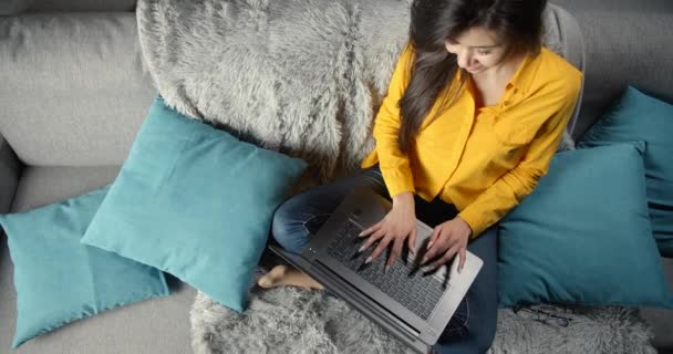 Vista superior de la chica sentada en el sofá y trabajando en el ordenador portátil — Vídeos de Stock
