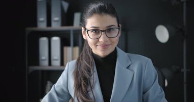 Ofiste gülümseyen ve kameraya bakan hoş bir bayan.