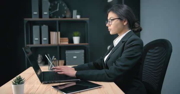 Vista lateral de la mujer de negocios sentada en el escritorio con computadora portátil — Vídeos de Stock