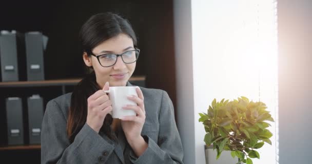 Glimlachende zakenvrouw in bril genietend van lekkere koffie — Stockvideo