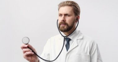 Steteskop kullanan, beyaz üniformalı olgun sakallı bir doktor.