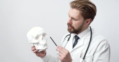 Bearded doctor in white lab with human skull