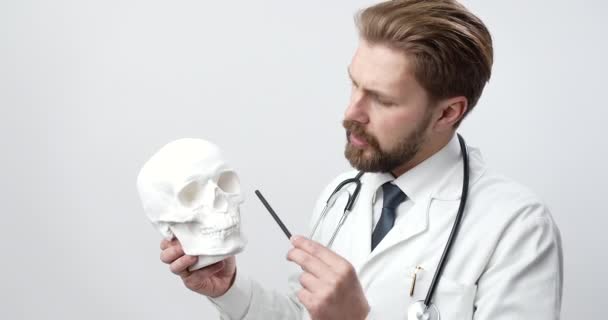 Bearded doctor in white lab with human skull — Stockvideo
