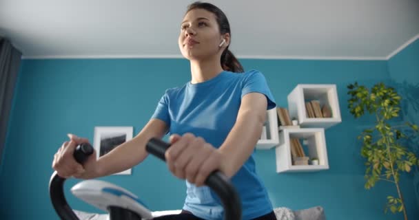 Fitness girl exercising on stationary bike at home — Stockvideo