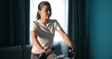 Active female looking at smart watch while riding static bike