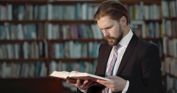 Человек в костюме читает книгу в библиотеке — стоковое видео