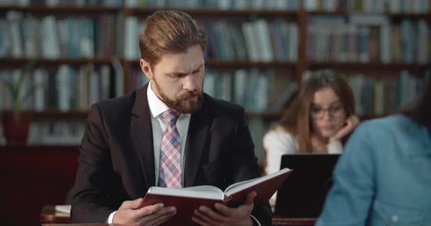 Estudiante masculino leyendo libro en la biblioteca — Vídeo de stock