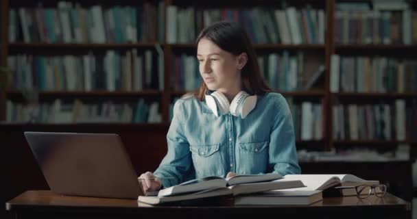 Студентка с ноутбуком читает в библиотеке — стоковое видео
