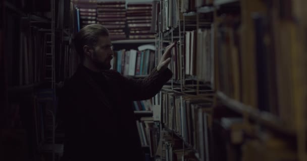 Человек выбирает книгу в темной библиотеке — стоковое видео