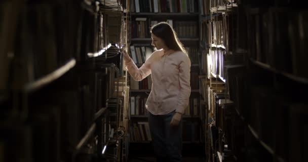 Женщина в поисках книги в темной библиотеке — стоковое видео