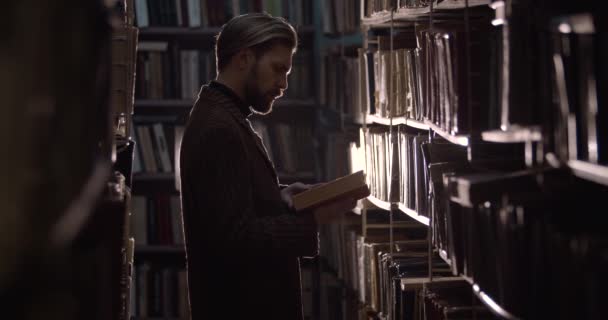 Homme barbu lisant un livre poussiéreux à la bibliothèque — Video