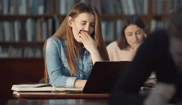 Yawning girl working laptop, library