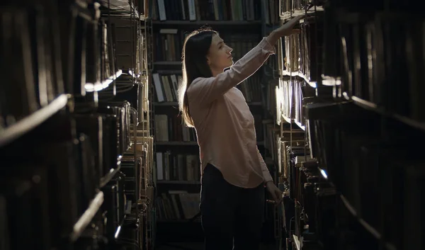 Girl looking for book in bookcase — Zdjęcie stockowe