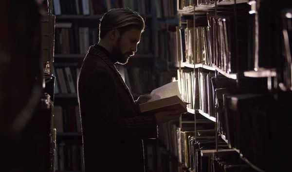 Man reading book, dark library — Stockfoto