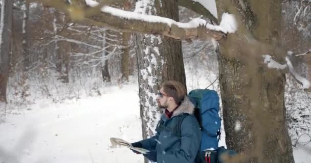 Uomo in piedi nella foresta durante la nevicata e guardando la mappa — Video Stock